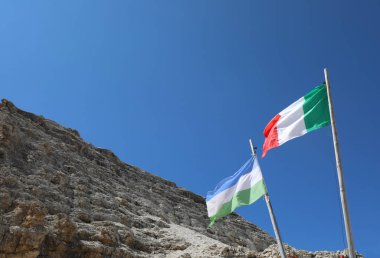 two flag one italian and on e of Ladinia Geographical Area the Alpine region in the Dolomites Zone of Northern Italy and the rocks of Mountain in summer clipart