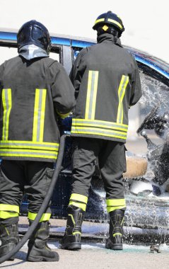 Trafik kazasından sonra iki itfaiyeci mavi bir arabaya köpük sıkıyor.