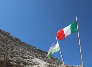 Italian flag and flag of Ladinia the Alpine region in the Dolomites Area of Northern Italy and the rocks of Mountain in summer clipart