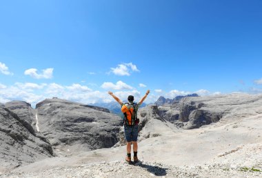 Sırt çantalı genç yürüyüşçü, İtalya 'nın kuzeyindeki Avrupa Alpleri' ndeki Dolomitler dağlarındaki Sasso Pordoi dağlarında zafer için kollarını kaldırıyor.