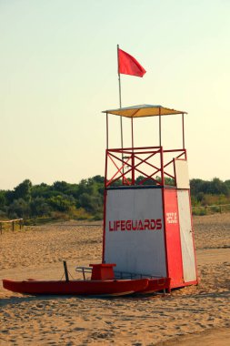 lifeguard tower with red flag flying high on sandy beach clipart