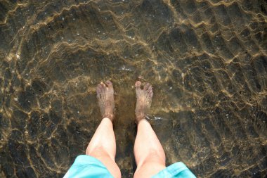Tatilde, bir yaz günü okyanusun sularında sırılsıklam olan bir adamın iki çıplak ayağı ve bacağı.