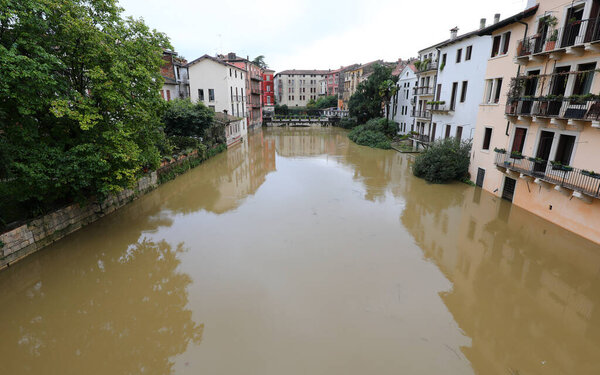 river in flood flowing through city streets surrounded by houses during flood caused by torrential rains