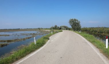 narrow asphalt road through plain with lagoon alongside without people clipart