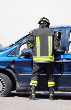 Araba kazası geçiren mavi arabaya acil durum müdahalesi sırasında koruyucu kasklı itfaiyeci.