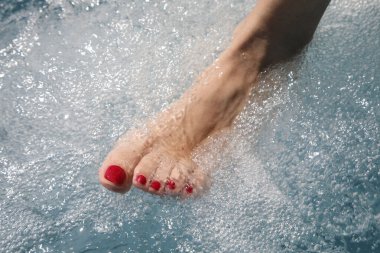 Tırnak cilasıyla süslenmiş kadın ayağı gıdıklanma ve masaj kabarcıklarıyla dolu suya batırılmış.