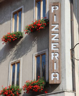 Büyük İtalyan tabelasının üzerinde pizzanın tipik İtalyan yemeğinin servis edildiği restoranı gösteren pizzacı yazısı var.
