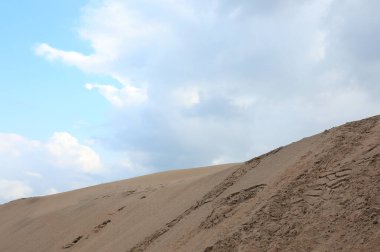 İnsansız kum tepeciğinin altından ve beyaz bulutlu gökyüzünden bak.