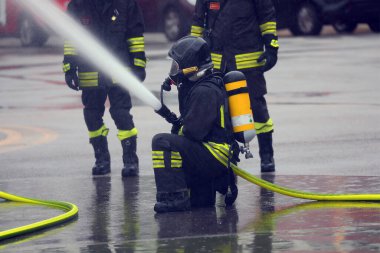 Firefighter with an oxygen tank and mask spraying a large amount of water during an emergency clipart