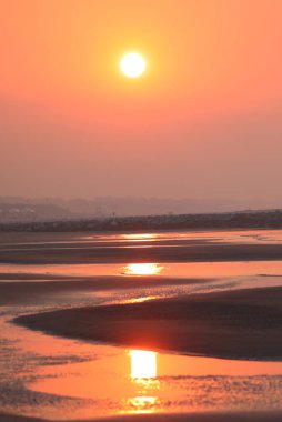 romantic background with large orange sun reflecting on sea water at shoreline without people clipart