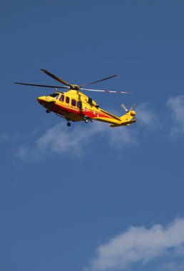 Canazei, TN, Italy - July 30, 2024: Yellow helicopter of italian fire departmnetair medical services flying in the blue sky clipart