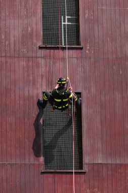Korunmak için kask ve kask takan cesur itfaiyeci halatlar ve güvenlik karabinalarıyla iniyor.