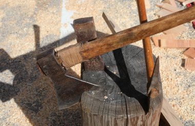 axes and hatchets embedded in a wooden stump at a wood processing company clipart