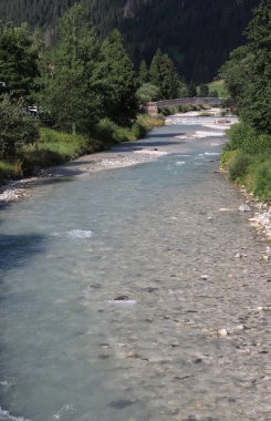 Erimiş kar suyuyla beslenen dağ deresi vadinin aşağısına doğru akıyor. Uzaktan görünen bir köprüyle.