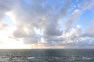 Gün batımında alçak bulutların arasından süzülen güneş ışığı ve Tanrı 'nın dini bir kavramı ya da doğal bir arkaplan olarak ideal, yumuşak dalgalarla aşağıdaki deniz.