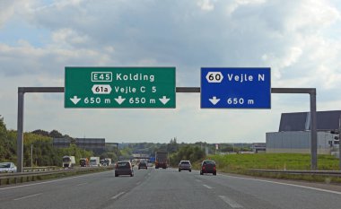 Kuzey Avrupa 'da Danimarka' daki şehirlere giden yol işaretleri ve oradan geçen arabalar.