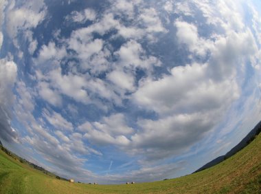 fisheye photograph of the blue sky and white clouds and the green meadow distorted by the curvature of the lens clipart