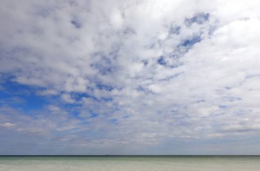 beautiful tropical seascape with the sea below and lots of white clouds contrasting with the blue sky clipart