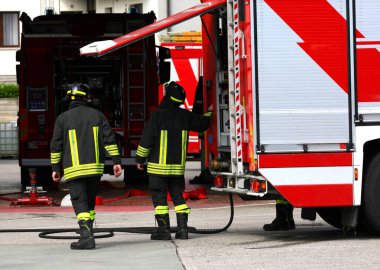 Acil müdahale sırasında koruyucu kasklı itfaiyeciler itfaiye aracından ekipmanları alıyor.