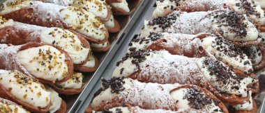 many Sicilian cannoli filled with ricotta cream and topped with pistachio and chocolate flakes for sale in the Italian pastry shop clipart