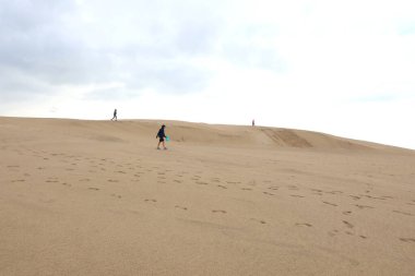 Çölde, uçsuz bucaksız kum tepesinde yürüyen üç kişi.