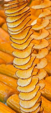 long skewers of fried potato chips with peel and yellow organic corn cobs  for sale in street food stall clipart