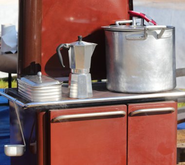 Kırsal bir mutfakta çok eski bir odun sobası tepesinde çömlekler ve ev yapımı kahve yapmak için büyük bir Moka demliği.