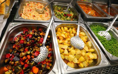 Mataranın servis restoranında patatesli, yeşil bezelyeli ve karışık sebzeli pilav dolu paslanmaz çelik tepsiler.