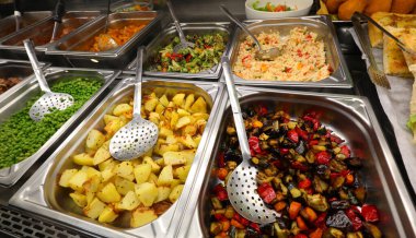 Kendi servis restoranının paslanmaz çelik tepsilerinde pişmiş sebzelerin geniş çeşitliliği