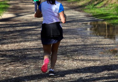 Şehir parkında spor kıyafetleri ve koşu ayakkabılarıyla koşan genç bir kadın.