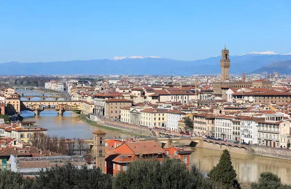 İtalya 'nın orta kesimindeki Floransa şehrinin panoramik manzarasında Arno nehri üzerindeki Ponte Vecchio ve Palazzo della Signoria ve arka planda karla kaplı Apennine dağları da dahil olmak üzere ünlü anıtlar var.
