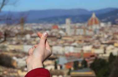 Baş parmak ve işaret parmağıyla, bulanık arkaplanda Kalbin ve İtalyan şehrinin Floransa işaretini oluşturur.