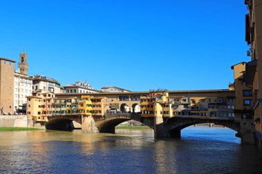 İtalyanca PONTE VECCHIO denilen eski köprü ve altından akan Arno nehri ve mavi gökyüzü.