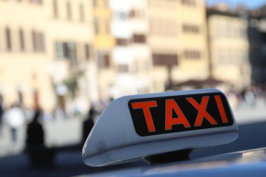 Şehir meydanında gezginleri bekleyen kırmızı Taxi yazan bir tabela var.