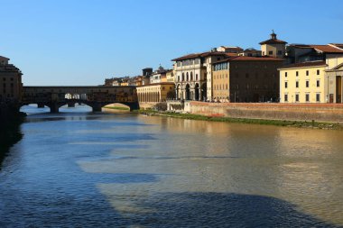 LUNGARNO 'nun geniş açılı manzarası, Arno nehrinin kıyısında binalar ve Ponte Vecchio ile birlikte yazın İtalya' nın orta kesimindeki Floransa şehrinde görülür.