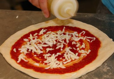 Pizza şefi çiğ pizzanın üstüne zeytinyağı koyuyor. Tipik İtalyan mutfağı ve kırmızı domates sosu.