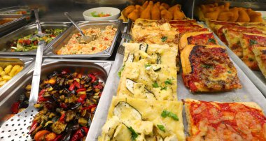 Sebze salatalı pizza ve Focaccia gibi sıcak yemeklerle dolu tepsiler.