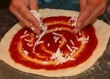 İtalyan mutfağının tipik pizza hamuru ve kırmızı domates sosunun üzerine mozzarella peyniri koyan pizza şefinin elleri.