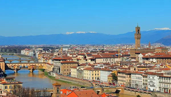 Kuzey İtalya 'daki Floransa şehrinin panoramik manzarası. Arno Nehri üzerindeki Ponte Vecchio ve Vecchio Sarayı ve açık mavi arka plandaki kar kaplı Apennines dağları.