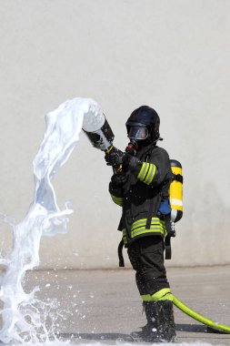 Büyük yangın hortumu, beyaz köpük ve koruyucu miğferi olan cesur itfaiyeci.