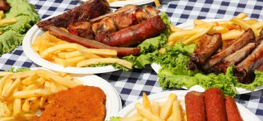 Köy festivali masasında masa örtüsü, patates kızartması, sosis ve domuz pirzolası.