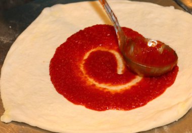 İtalyan pizza hamuru ve domates sosu metal bir kepçeyle eşit olarak yayılmış.