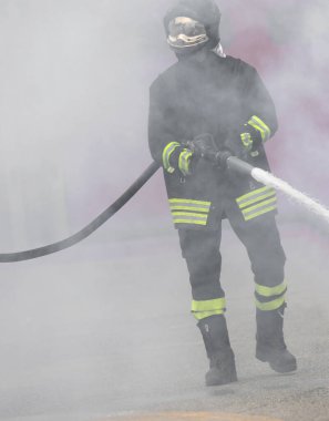 Yangın söndürme sırasında beyaz duman ortasında yangın hortumu ile itfaiyeci