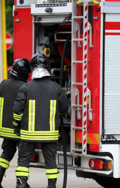 Acil durum yönetimi ve itfaiye kamyonu sırasında koruyucu kasklı ve üniformalı itfaiyeciler.