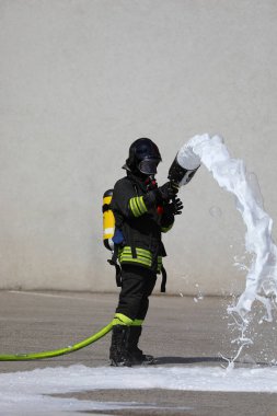 Büyük yangın hortumu, beyaz köpük, koruyucu miğfer ve oksijen tüpüyle cesur itfaiyeci.