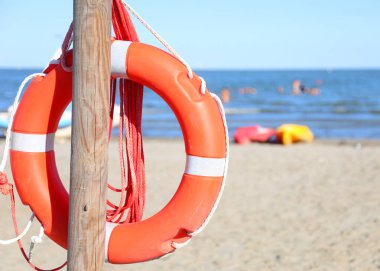 Turuncu can yeleği, kumlu sahilde tahta bir direğe asılı duran dayanıklı plastikten yapılmış. Cankurtaranların denizdeki insanları kurtarması için kullanılabilir.