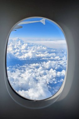 Beyaz bulutlar ve mavi gökyüzü. Kıtalararası bir uçuş sırasında pencereden bir uçak kanadı.