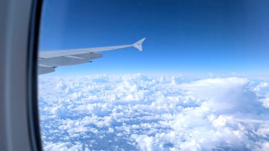 -- Uçak kanadı beyaz bulutlu küçük pencere penceresinden görünüyor.