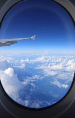Uçak penceresinin çerçevesi ve dışı kanat ve gökyüzü bulutlarla birlikte seyahat konsepti olarak görülür.