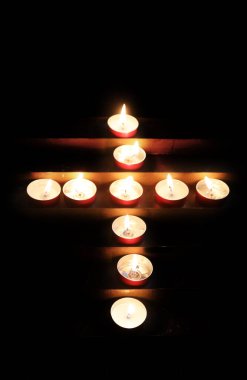 Karanlık bir sığınağa karşı haç şeklinde dizilmiş pek çok yanan dua mumu var.